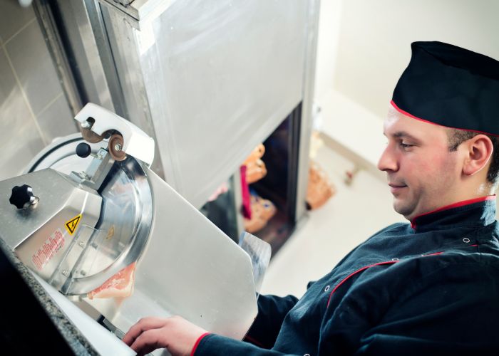 a chef slicing meat in an industrial meat slicer