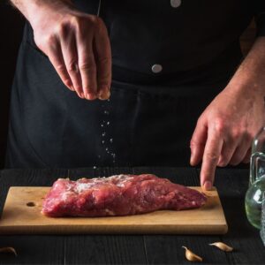 person salting a slab of meat