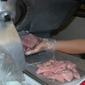 person catching meat coming out of a meat slicer