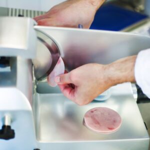 person removing a slice of meat from an automatic slicer